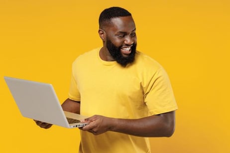 A man holding a laptop and looking over his shoulder, smiling, on a yellow background