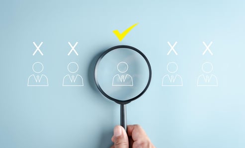 5 drawings of people in suits, 4 have crosses over their heads, one is being highlighted with a magnifying glass and has a tick over their head.